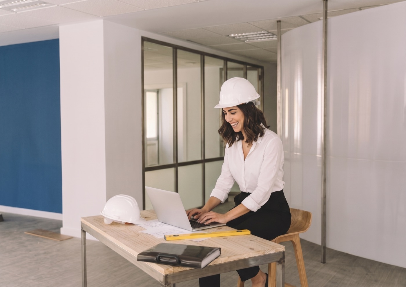 Arquitecta con casco trabajando en una laptop dentro de una oficina en obra